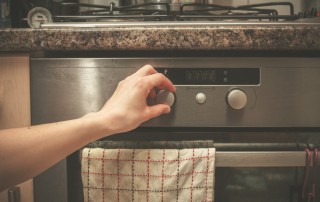 A woman cooking, turning a metal hand knob on an oven.